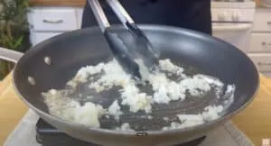 Sautéing chopped onions in a skillet with black tongs for a delicious recipe preparation.